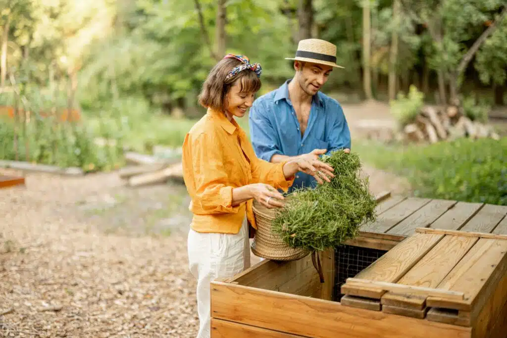 Couple throwing cut grass to compost wooden bin